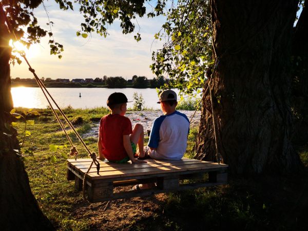Zwei Jungen auf einer Holzschaukel mit Blick auf den Sonnenuntergang beim Camping an der Elbe