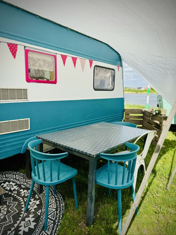 White turquoise retro camper with sitting area and awning right on Stover Strand Camping in Hamburg