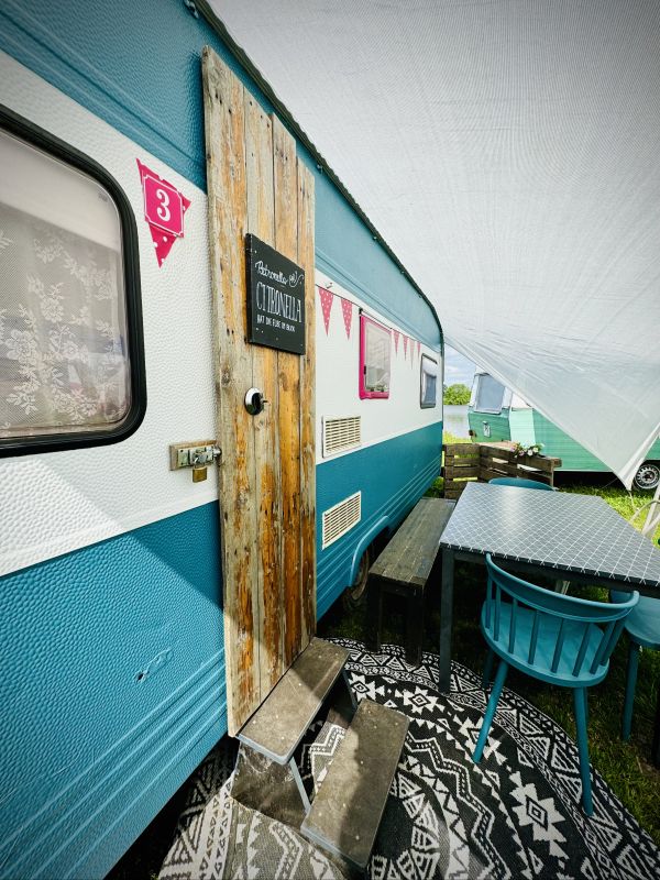 White turquoise retro camper with a cozy outdoor sitting area right on Stover Strand Camping